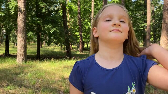 Portrait lovely pre-teen girl in the great outdoors on sunny day. Beautiful female child lets her blonde hair down looking at camera while family camping in forest. Delightful kid poses for best shot