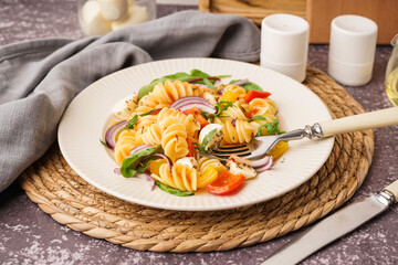 Plate of tasty pasta salad with pepper and red onion on dark table