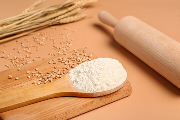 Spoon with flour and wheat grains on beige background, closeup