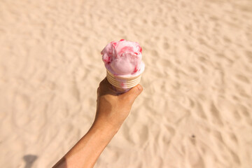 Hand holding ice cream cone on the beach in summer day.