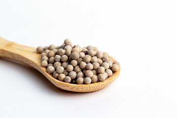 White pepper seeds in wooden spoon isolated on white background.