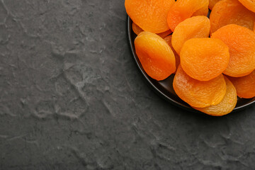 Tray with tasty dried apricots on black background