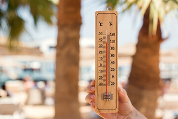 Thermometer in hand on a beach background showing high temperature. Hot weather and climate concept
