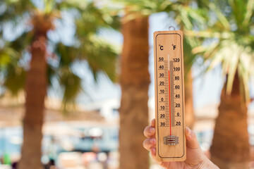 Thermometer in hand on a beach background showing high temperature. Hot weather and climate concept