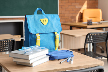 Blue school backpack with stationery and eyeglasses on desk in classroom
