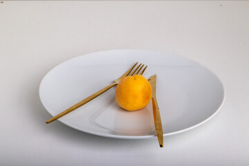 golden fork with a knife and lie together with an apricot on a white plate on a white background