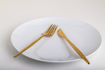 golden fork with a knife lie on a white plate on a white background
