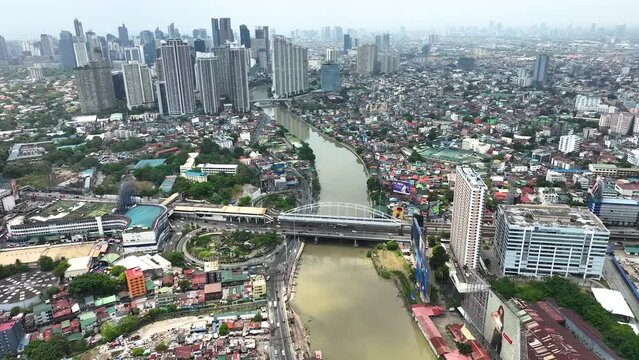 Manila cityscape at river banks aerial. Downtown area with cottages, skyscrapers, buildings. Urban Philippines city scape with streets and roads. Town drone shot. Poor Homes Along Rich Skyscrapers.