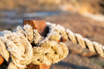 Rope with frost  tied to shore to anchor a vessel, nautical theme. rustic pillar and the sea in the background on a sunny winter day. 