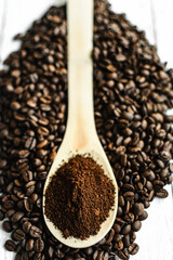 ground coffee in a wooden spoon on a slide of medium-roasted coffee beans on a light background