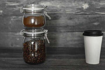 Obraz na płótnie Canvas ground coffee and beans in glass jars. white cup for coffee and tea on a dark background