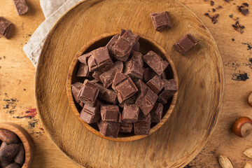 Cubes of organic milk chocolate in a wooden bowl on a wooden background.