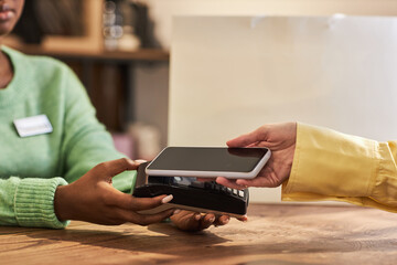 Side view closeup of unrecognizable young woman paying via smartphone NFC technology in store, copy space