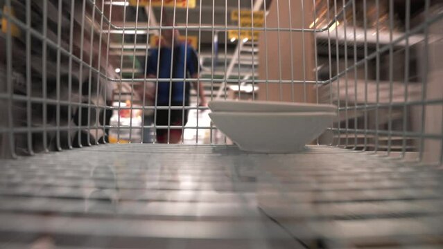 Timelapse close up view the buyer puts the dishes in the stainless steel shopping cart in a furniture and kitchenware store. Moving Into a New Apartment.