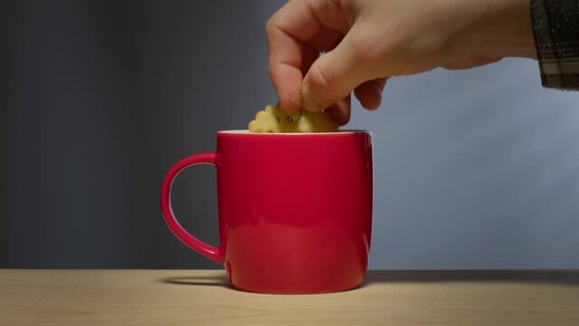 A man's hand dunks a biscuit - cookie - into a hot beverage in a bright red coffee mug.