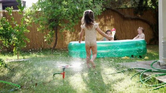 A Little Baby Girl in a Bathing Suit has Fun and Plays with a Watering Hose