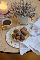 Fototapeta na wymiar Vegan candies with nuts, raisins, dates, cocoa, coconut oil. Useful healthy homemade dessert without gluten, sugar, eggs, butter. Sweet food. Cozy mood. Cup of tea, potted plant, candle in a frame. 