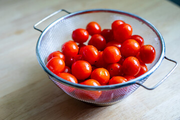 Fresh red ripe cherry tomatoes in a basket on a wooden table, prepare for cooking.