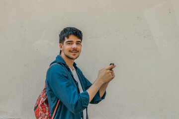 young man with mobile phone and backpack isolated on wall in the street outdoors