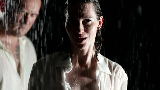 Portrait of a pretty adult woman standing wet in the rain at night in an excited state. In the background, a brutal bald man approaches her