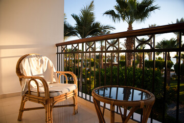Rattan chair and coffee table on the hotel terrace with palm trees at sunset, luxury tropical vacation no people