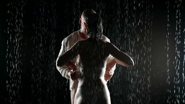 Lovers in the pouring rain at night stand and hug a man slowly undresses his woman
