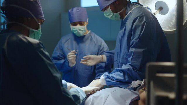 Team professional surgeons and nurses in uniform at work in operating room,performing heart transplant surgery operation under bright lamps and looking at screen.Teamwork surgeon in operating room