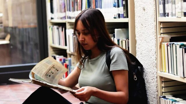 young student woman reading a book in a library at a university in colombia