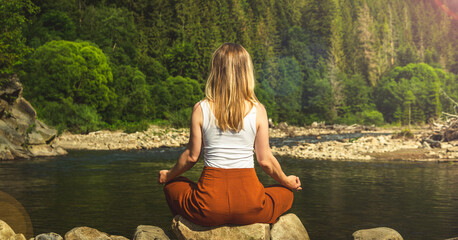 Woman doing yoga on the stone at the mountain river. Carpathians