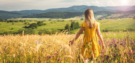 Woman in yellow dress staying at the green meadow in the mountain