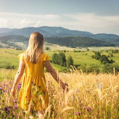 Obraz premium Woman in yellow dress staying at the green meadow in the mountain