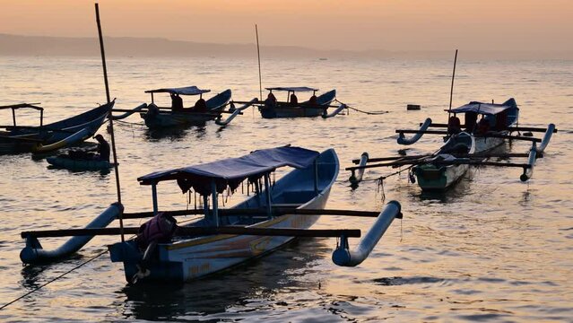 Fishing boats moored and rocked by the waves in the morning at Pangandaran beach before sunrise with fog and small boats seen in the distance. Medium shot and handheld.