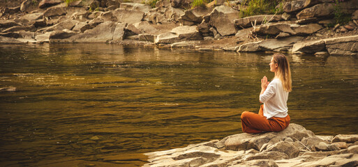 Woman doing yoga on the stone at the mountain river. Carpathians