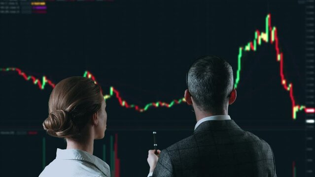 Colleagues traders are working with multiple computer screens full of charts and data analysis and stock broker trading online. Back view. Concept of bitcoin and stock market trading.