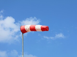 Windsock indicator of wind. Horizontally flying windsock ( wind vane ) with blue sky and white clouds in  the background. Wind cone indicating wind and force.