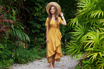 Young woman in a stylish summer dress enjoys the beauty of a tropical resort, walking among palm trees and embracing the vacation vibes. Concept of travel and summer relaxation.