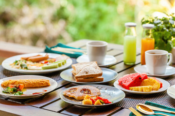 Breakfast table near lake in Asian resort. Delicious and healthy meal with fresh tropical fruits, sandwiches and organic coffee. Concept of a Thailand vacation.