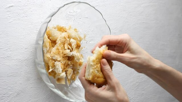 Puff pastry is torn into pieces by female hands. Cooking Umm Ali, delicious arabic dessert or bread pudding on light gray table