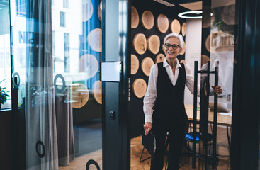 Positive senior woman in classy suit leaving conference room