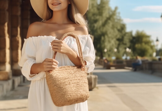 Young woman wearing white dress with stylish straw bag in street.