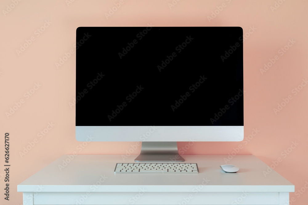 Wall mural mockup computer monitor with a keyboard on a table against a pink wall.