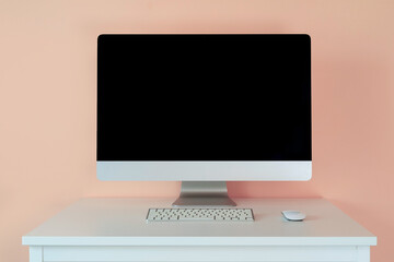 Mockup computer monitor with a keyboard on a table against a pink wall.