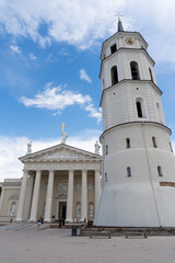Vilnius Cathedral, with people walking through the square, on a day with a blue sky and some clouds.