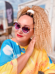 Portrait of pretty woman with curly blond hair in a bright yellow blouse and sunglasses  in Jurmala, Latvia. Summer travel and vacation concept.