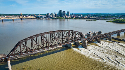 Aerial truss arch bridge over Ohio River rapids from dam Louisville Kentucky skyscrapers on horizon