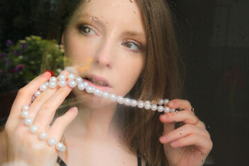 portrait einer jungen blonden frau, die mit einer perlenkette spielt - obrazy, fototapety, plakaty