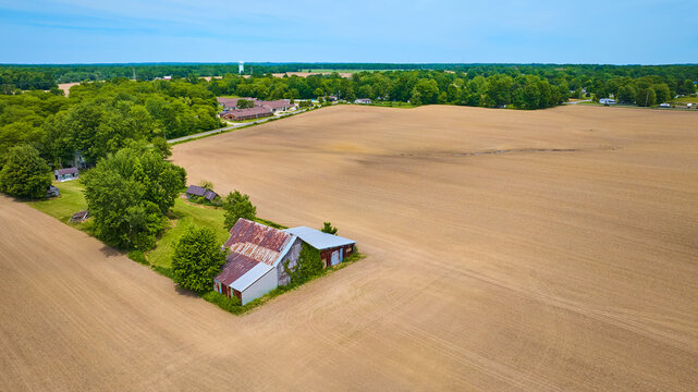 High up aerial view of empty dirt farmland with brown scar on land and old rusting barn