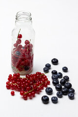 Summer berry drink in a bottle. Sprigs of red currant and blueberries on the table.