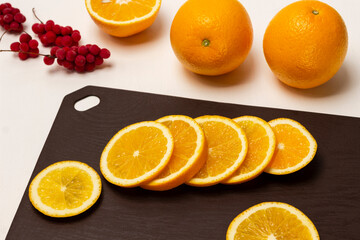Slicing an orange on a cutting board. Two whole oranges.
