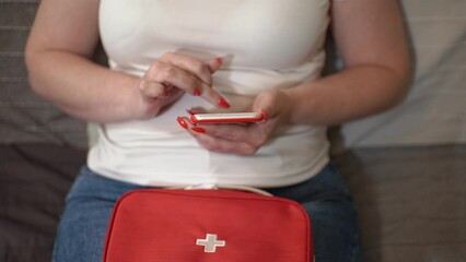 a woman holds a smartphone in her hand. woman writes a message to the doctor. woman and first aid kit. close-up of a red smartphone. Quality footage in Full HD
